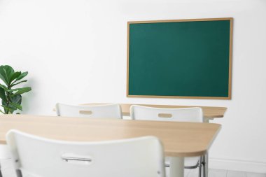 Boş yeşil karatahta, masalar, sandalyeler ve bitkiler sınıfta