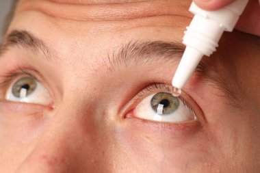 Göz damlası süren genç adam, yakın çekim görüntüsü.