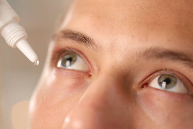 Bulanık arkaplanda göz damlası uygulayan adam, yakın plan