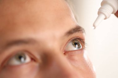 Işık arkaplanına göz damlası uygulayan adam, yakın plan