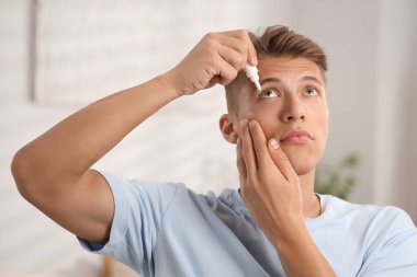 Evde göz damlası kullanan genç bir adam.