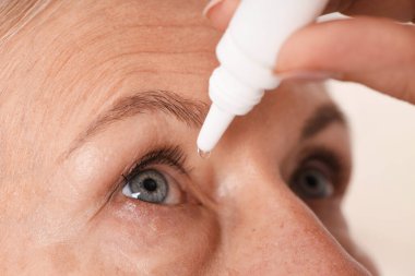 Işık arkaplanına göz damlası uygulayan kadın, yakın plan