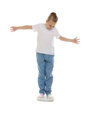 Küçük kız beyaz arka planda terazide duruyor.