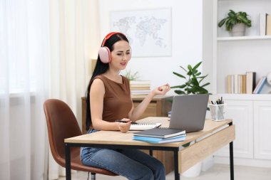 Kulaklıklı bir kadın bilgisayarla kapalı bir masada çevrimiçi sınavdan geçiyor.