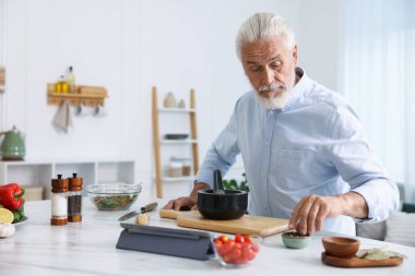 Mutfaktaki beyaz mermer masada yaşlı bir adam yemek pişiriyor.