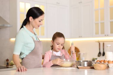 Küçük yardımcı. Anne ve kızı mutfaktaki beyaz mermer masada birlikte yemek pişiriyorlar.