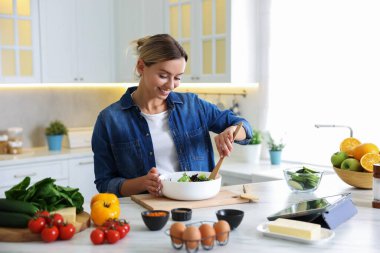 Mutfaktaki masada yemek yapan gülümseyen kadın.