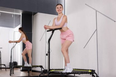 Spor salonundaki aynanın yanındaki trambolinde gülümseyen kadın, düşük açı.