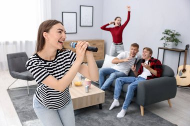 Genç bir kadın evde arkadaşlarıyla karaoke yapıyor, seçici odaklı.