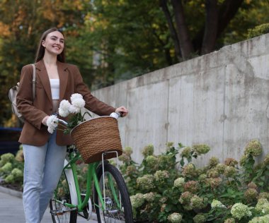 Dışarıdaki sepetin içinde çiçeklerle bisikletini gezdiren bir kadın. Metin için boşluk