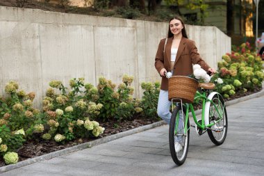 Dışarıdaki sepetin içinde çiçeklerle bisikletini gezdiren bir kadın. Metin için boşluk