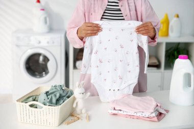 Beyaz masa içinde temiz bebek kıyafetleri katlayan kadın, yakın plan.