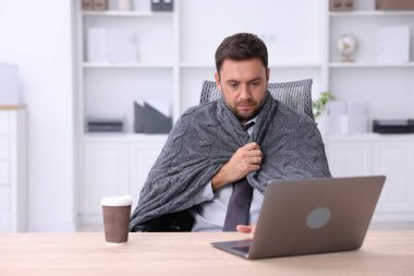 Klima. Ofiste battaniyeli bir adam soğuk hava yüzünden acı çekiyor.