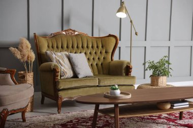 Oturma odasındaki gri duvarın yanında yumuşak kanepe, masa, koltuk ve lamba. İç tasarım