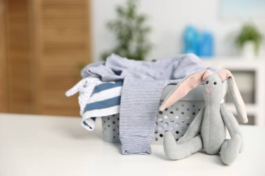 Çamaşır sepetinde bebek kıyafetleri ve beyaz masa üzerinde oyuncak tavşancık. Metin için boşluk