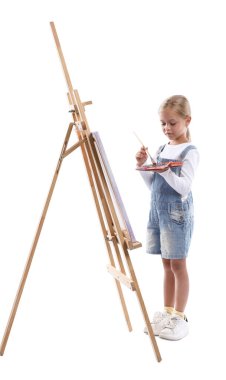 Meslek seçimi. Beyaz arka planda ressammış gibi davranan palet boyalı ve sehpanın yanındaki fırçalı küçük kız.