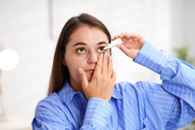 Evde göz damlası süren genç bir kadın.