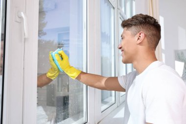 Evdeki paçavrayla pencereyi temizleyen adam.