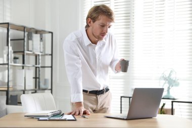 İçerde dizüstü bilgisayarı olan bir adam masanın yanında içki tutuyor.