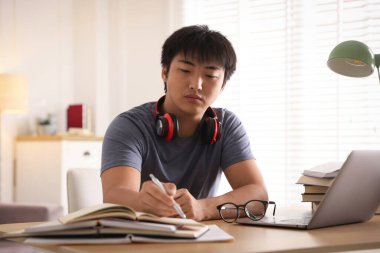 Bilgisayarlı bir öğrenci ve kapalı bir masada sınava hazırlanan kitaplar.