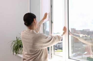 Genç bir kadın evinde modern bir pencere açıyor.