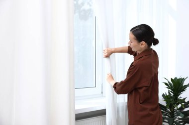 Kadın perdeleri açıyor ve pencereden dışarı bakıyor.