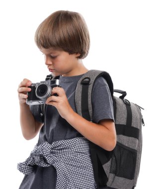 Meslek seçimi. Kameralı ve sırt çantalı küçük çocuk beyaz arka planda fotoğrafçı gibi davranıyor.