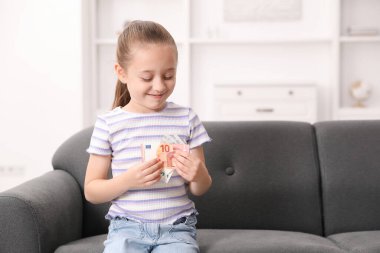 Evdeki kanepede cep harçlığı olan küçük kız, mesaj atmak için yer.