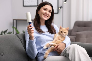 Tiftik silindirli gülümseyen kadın ve kedisi evdeki kanepede.