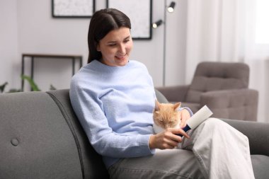 Tiftik silindirli gülümseyen kadın evdeki kanepede kedisinin saçlarını temizliyor.