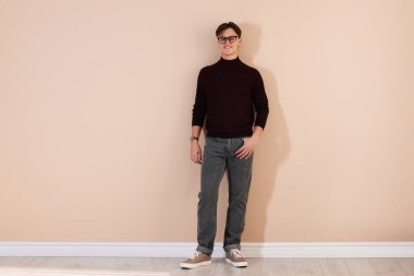 Bej duvarın yanında şık kotlu bir adam var.