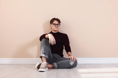 Bej duvarın yanında şık kotlu bir adam var.