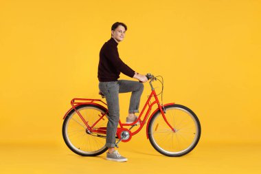 Turuncu arka planda kırmızı bisiklet süren yakışıklı bir adam.