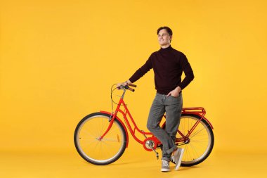 Turuncu arka planda kırmızı bisikletli yakışıklı bir adam.