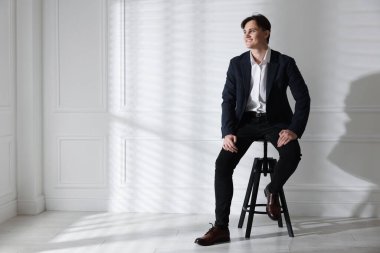 Beyaz duvarın yanındaki taburede şık kotlu adam, mesaj için yer var.