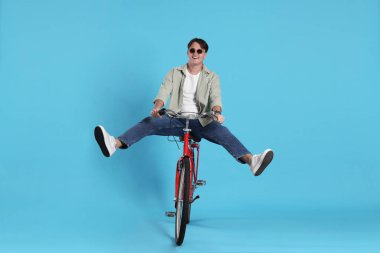 Açık mavi arka planda kırmızı bisiklete binen yakışıklı adam