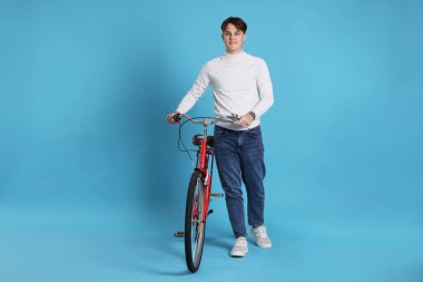 Açık mavi arka planda kırmızı bisikletli yakışıklı bir adam.