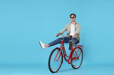 Açık mavi arka planda kırmızı bisiklete binen yakışıklı adam, metin için boşluk