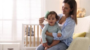 Anne bebeğinin saçını evde koltukta tarıyor.