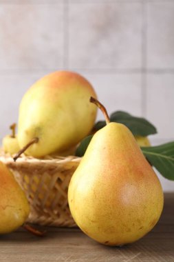 Yeşil yapraklı taze armutlar ve ahşap masadaki hasır sepet açık gri fayanslı duvara yakın çekim.