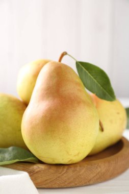 Taze armutlar ve yeşil yapraklar beyaz ahşap masada, yakın plan.