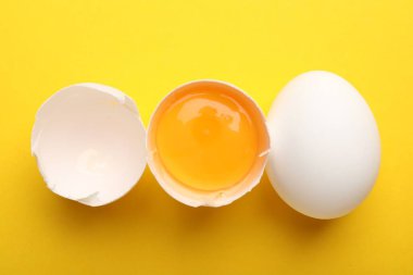 Whole and broken chicken eggs on yellow background, flat lay