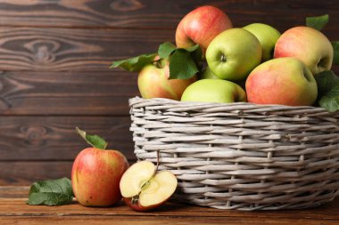 Tahta masadaki sepetin içinde yeşil yapraklı taze elmalar, yakın plan.