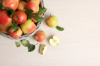 Taze olgun elmalar, hasır sepetin içinde yeşil yapraklarla beyaz ahşap masa, üst manzara. Metin için boşluk
