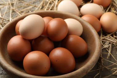 Tabakta çiğ tavuk yumurtası ve ahşap masada saman, yakın plan.