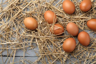 Raw chicken eggs and straw on grey wooden table, flat lay