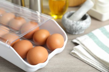 Plastik kabın içinde çiğ tavuk yumurtası ve ahşap tezgahın üzerinde mutfak aletleri, yakın plan.