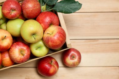 Sandıkta taze elmalar ve ahşap masada yeşil yapraklar, üst manzara. Metin için boşluk