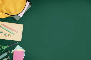 Öğretmenler günün kutlu olsun. Yeşil arka planda sırt çantası ve kırtasiye malzemesi. Metin için boşluk