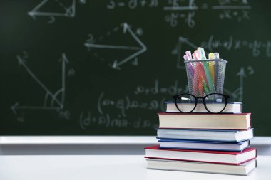 Öğretmenler günün kutlu olsun. Kara tahtaya karşı beyaz masada kitaplar, bardaklar ve kırtasiye malzemeleri. Metin için boşluk